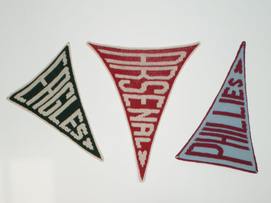 Three triangular KNIT flags with 'Eagles', 'Arsenal', and 'Phillies' text on a white background