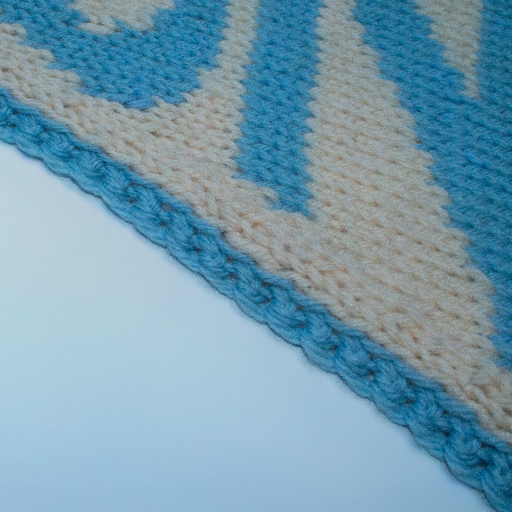 Close-up detail of a blue and beige handknit pennant with a graphic design containing the word "ANGEL" on a white background