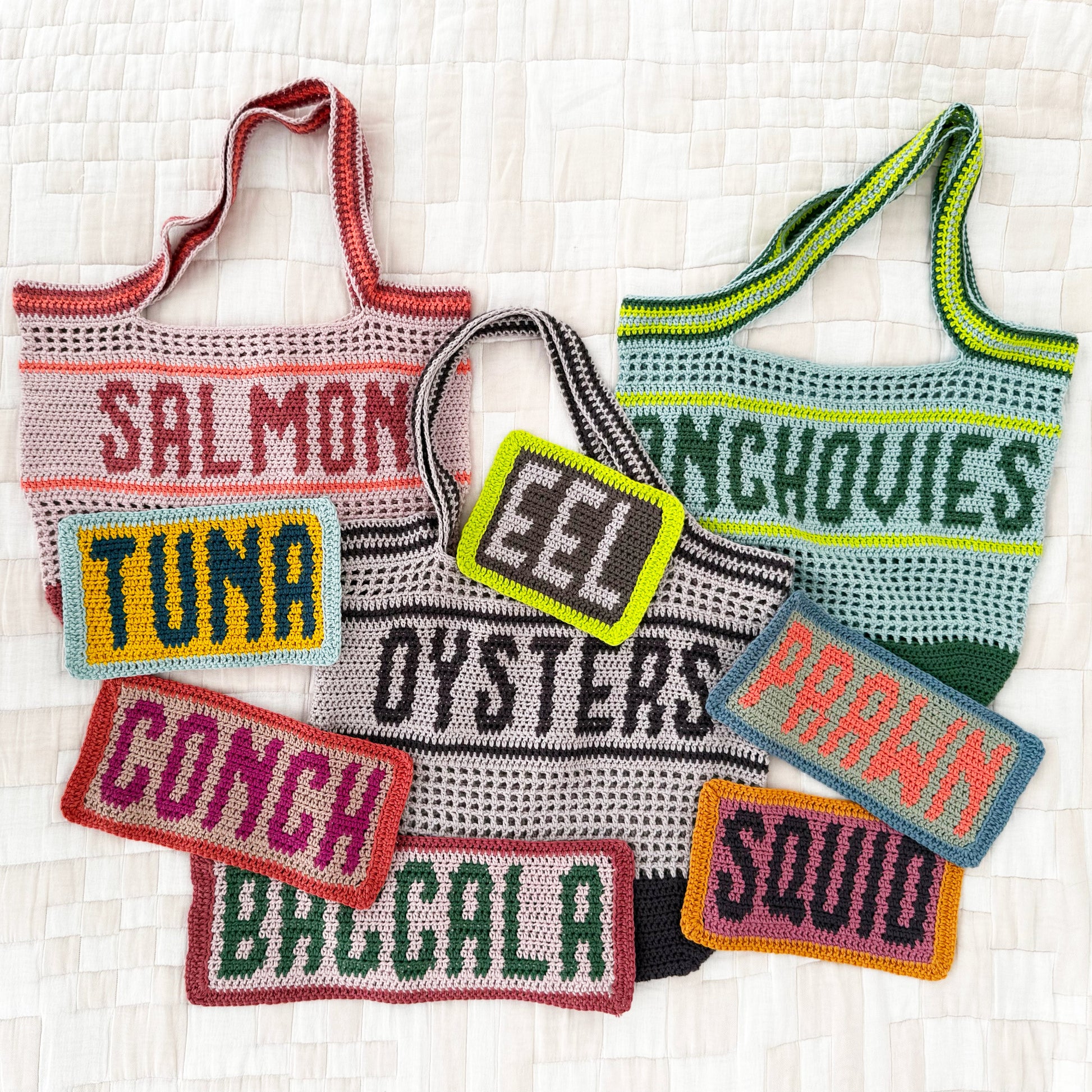 Crocheted tote bags and fish-themed patches on a textured white background