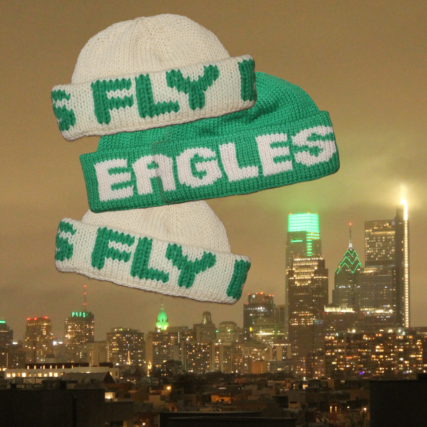 Four green and white beanies that say FLY EAGLES flying over the city of Philadelphia which is lit up green for its football team