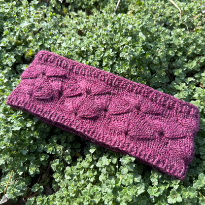 Purple knitted headband on green clover background featuring a fleabane flower motif