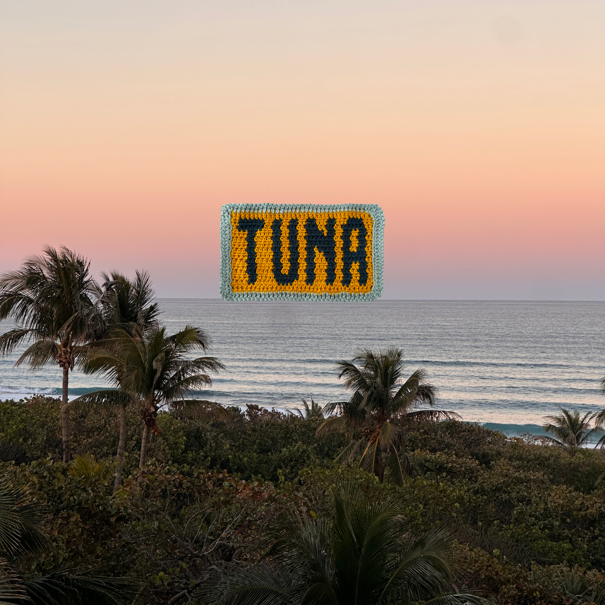 Crochet piece with 'TUNA' on a beach at sunset