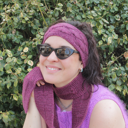 Woman wearing a purple knit headband and scarf both featuring a fleabane flower motif against a green leafy background