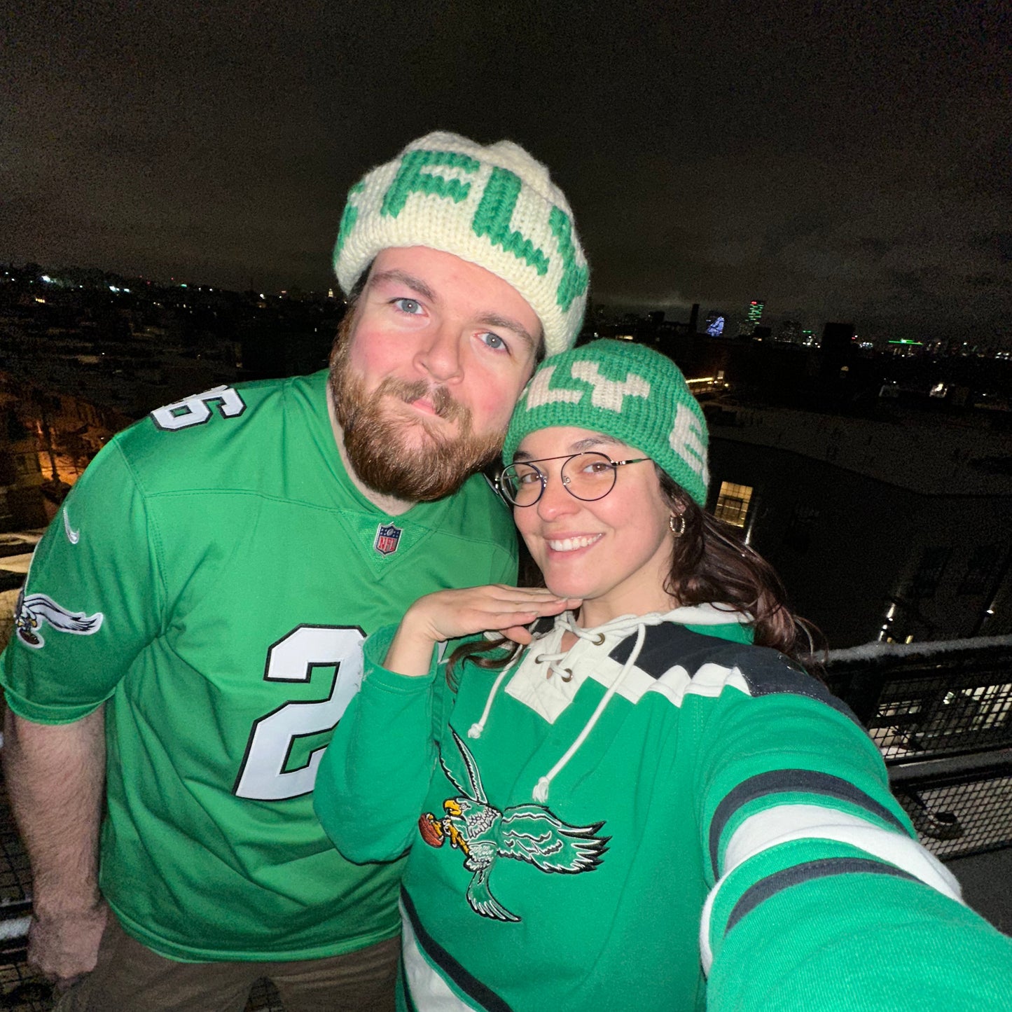 A selfie of a man and a woman wearing kelly green and white beanies that have the word FLY