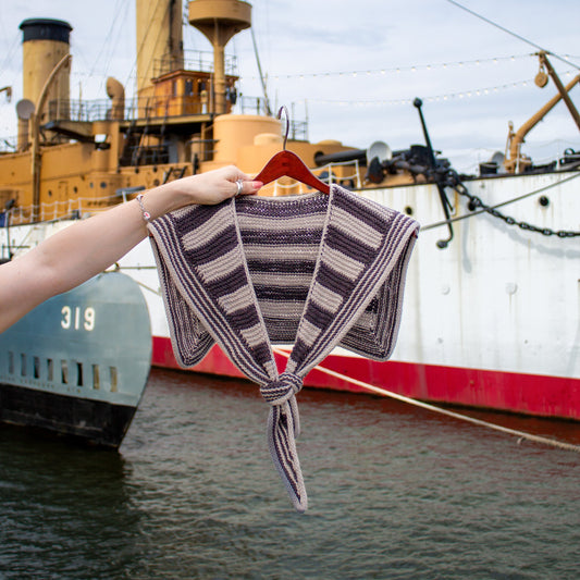 Knitted striped sailor scarf on a hanger with a large ship in the background