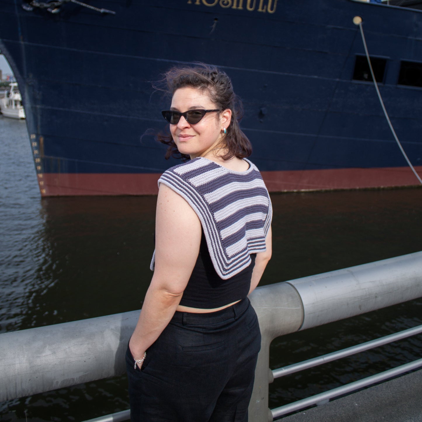 Woman standing in front of a large ship named 'Moshulu' on a dock wearing striped handknit sailor scarf.