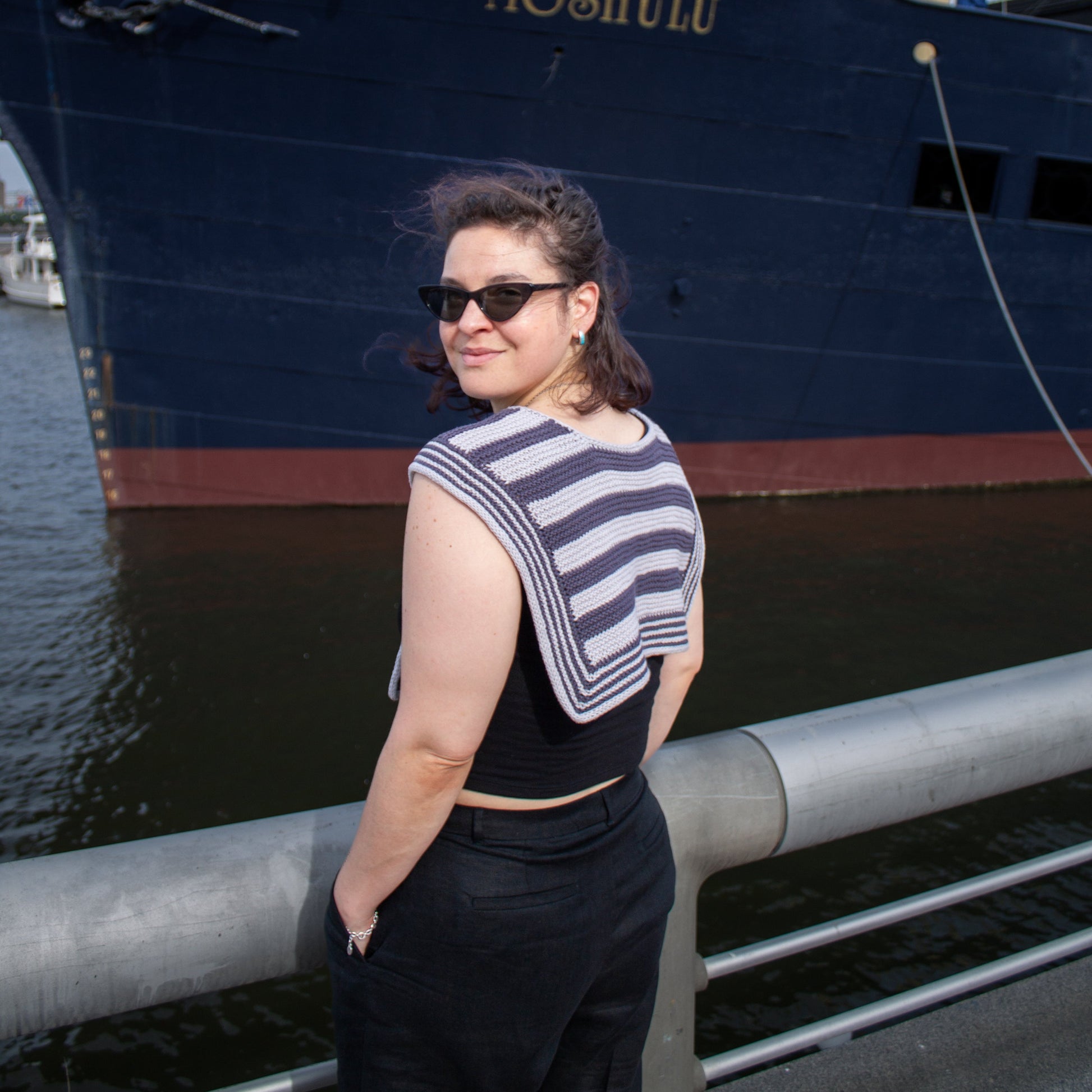 Woman standing in front of a large ship named 'Moshulu' on a dock wearing striped handknit sailor scarf.