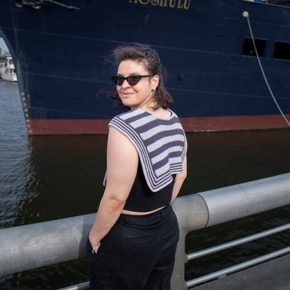 Woman standing in front of a large ship named 'Moshulu' on a dock wearing striped handknit sailor scarf.
